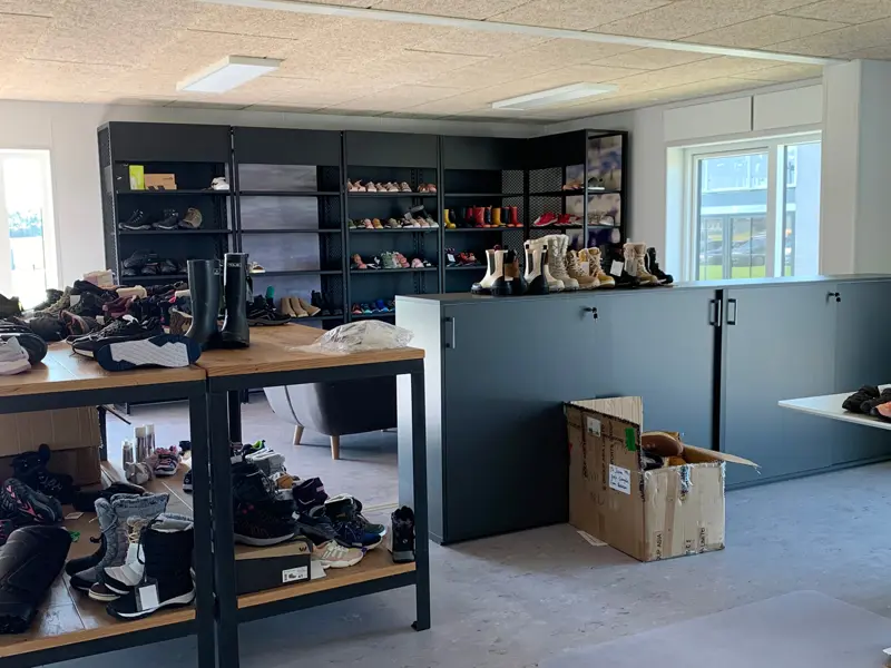 Et fremvisningsbord midt i lokalet med en masse sko på. På bagvæggen er der sorte reoler med sko på