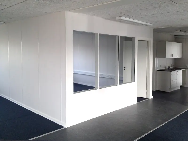 Et mødelokale integreret i kontoret, der er vinduer ind til lokalen. Længere bag i kontorlokalet er der et lille tekøkken.