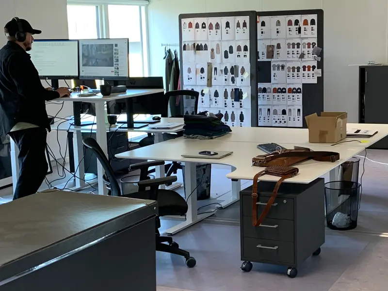 En mand står med headset på ved et hævet kontorbord. Flere kontorborde omkring, som bruges til at lægge ting fra sig på.